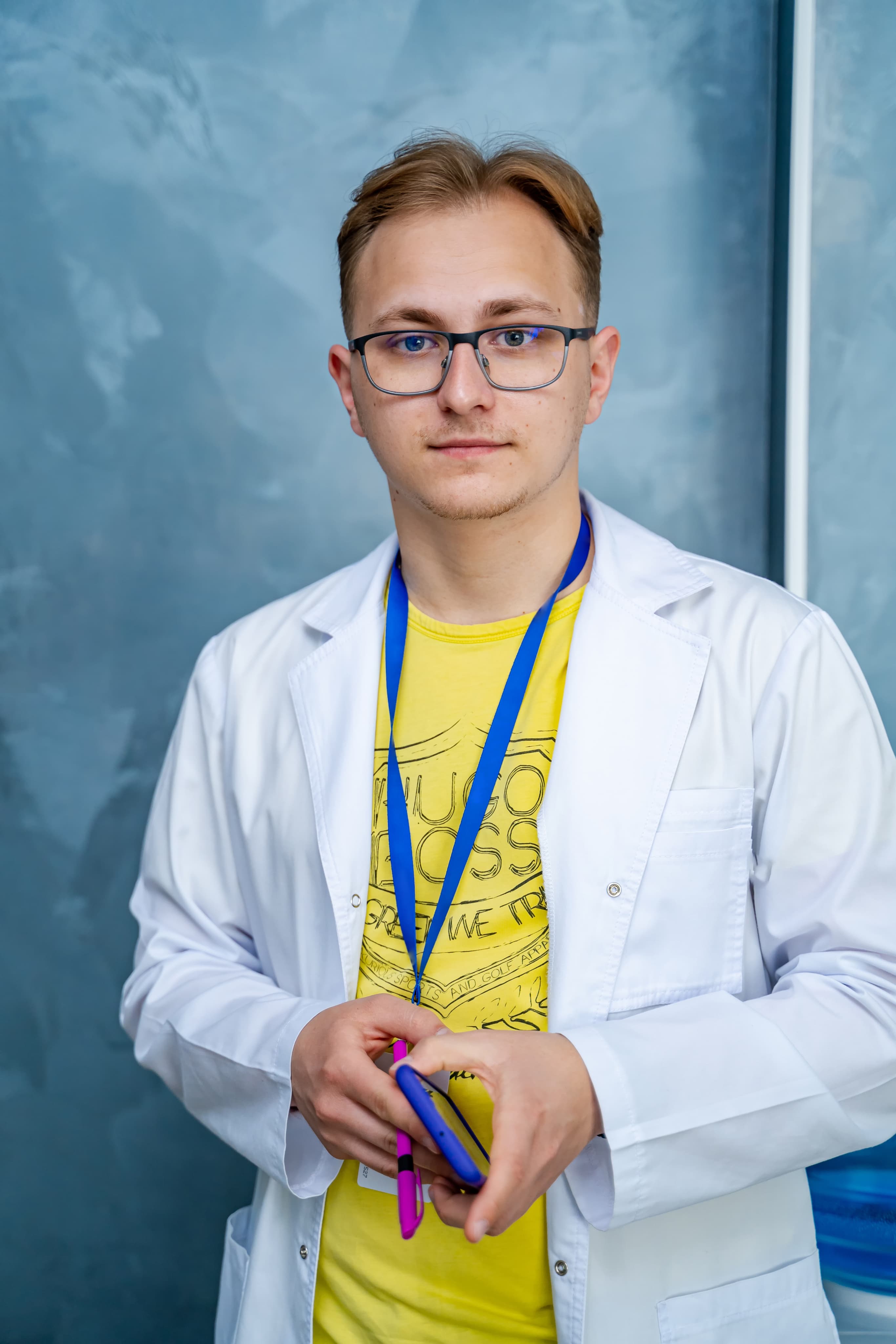 Nastolatek w białym fartuchu z identyfikatorem i telefonem w ręku, profil medyczny przygotowujący do zawodów lekarza i ratownika.