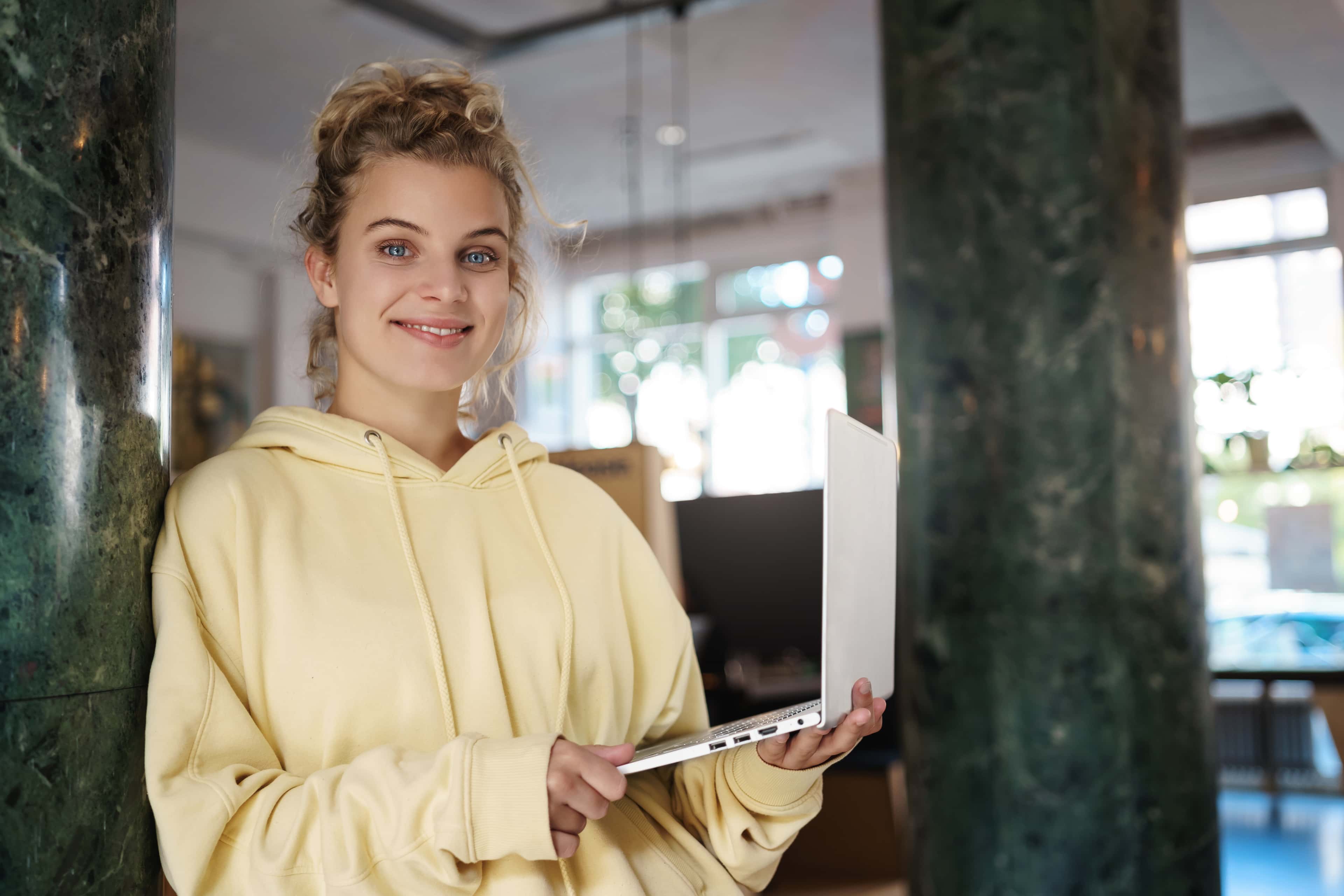 Uśmiechnięta studentka zdalnej szkoły IT z laptopem w przestrzeni coworkingowej