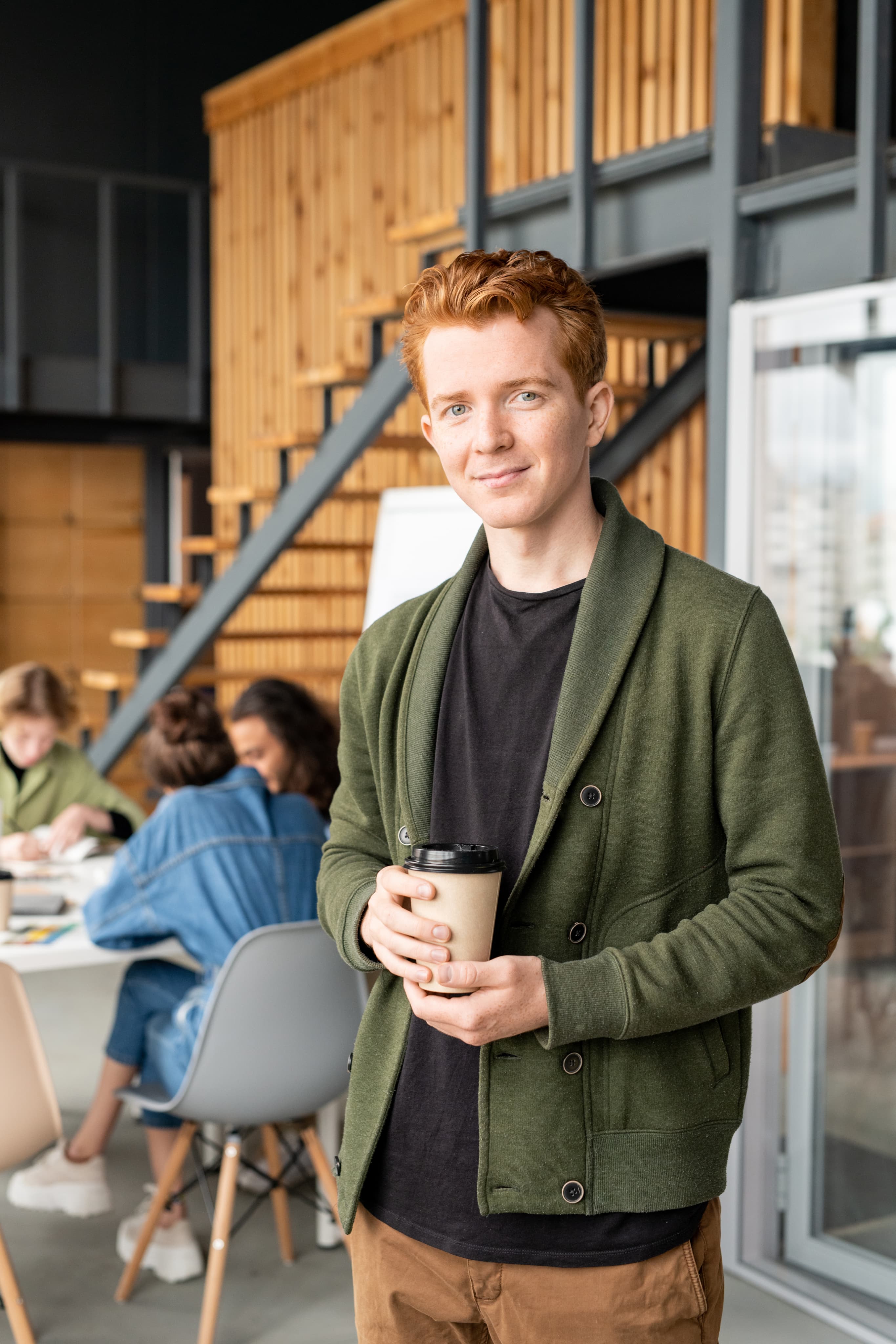 Chłopak z kubkiem kawy na tle nowoczesnego biura, profil startupowy i przedsiębiorczy.