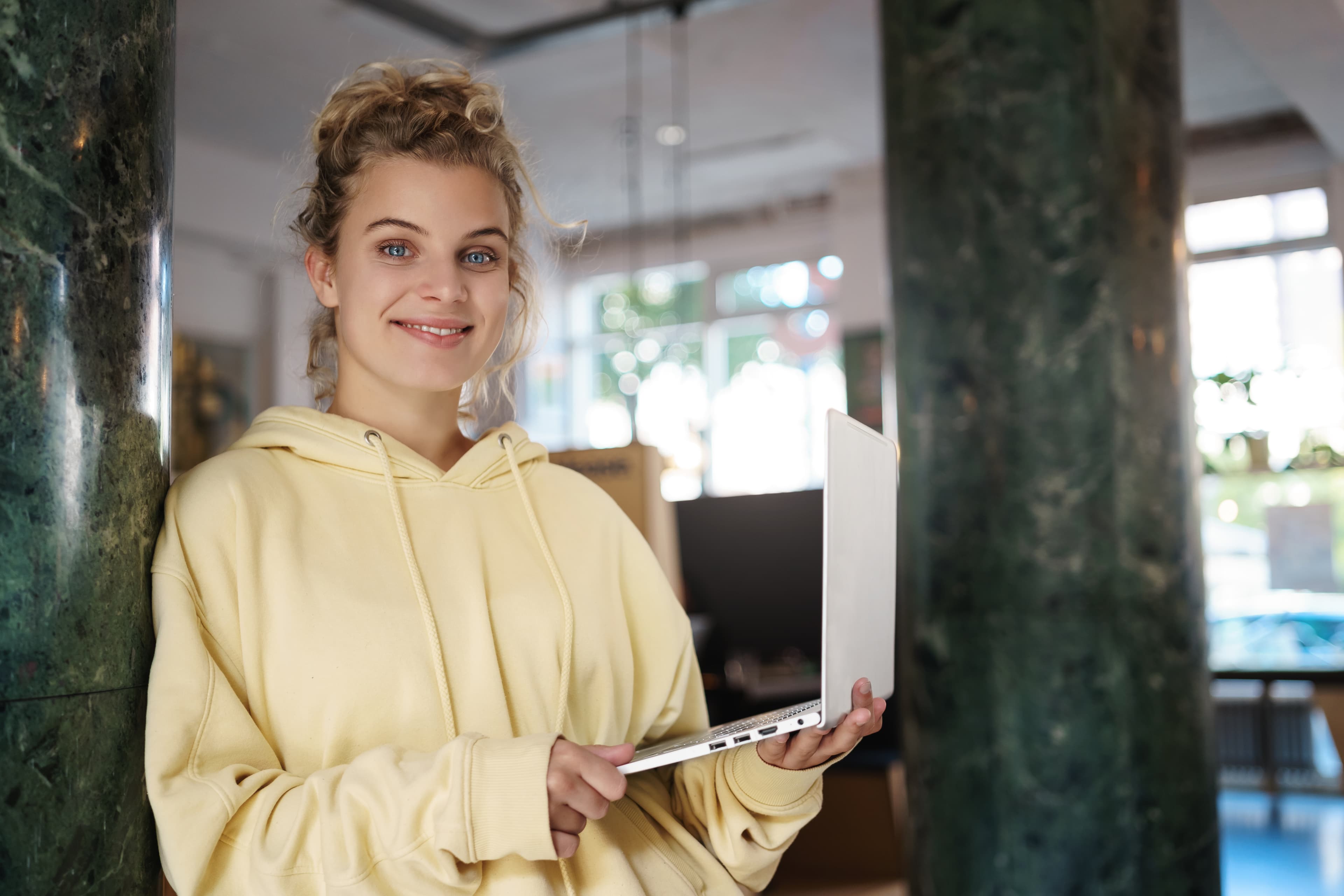 Uśmiechnięta studentka zdalnej szkoły IT z laptopem w przestrzeni coworkingowej