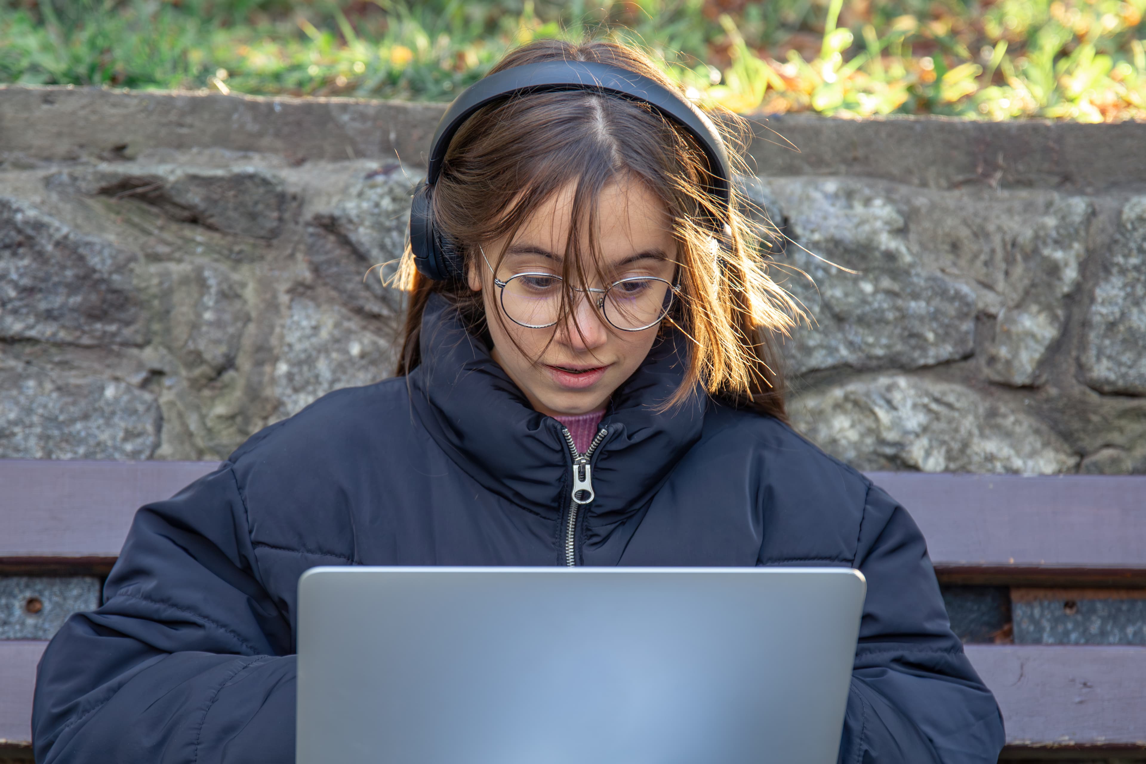 Uczennica szkoły zdalnej ze słuchawkami pracuje na laptopie na świeżym powietrzu