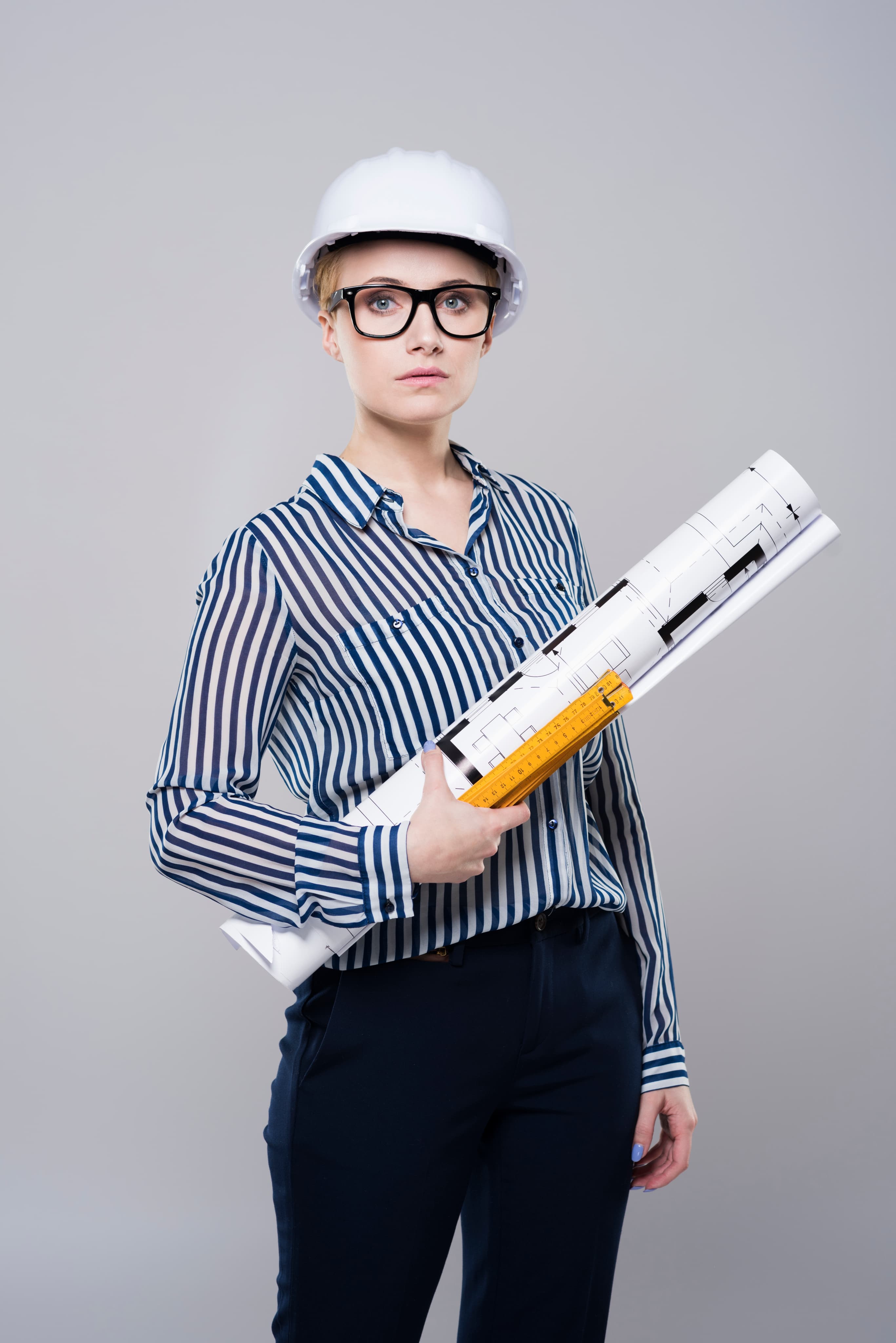 Dziewczyna w kasku ochronnym trzymająca zwinięte plany i linijkę, profil politechniczny z zainteresowaniem architekturą i inżynierią.